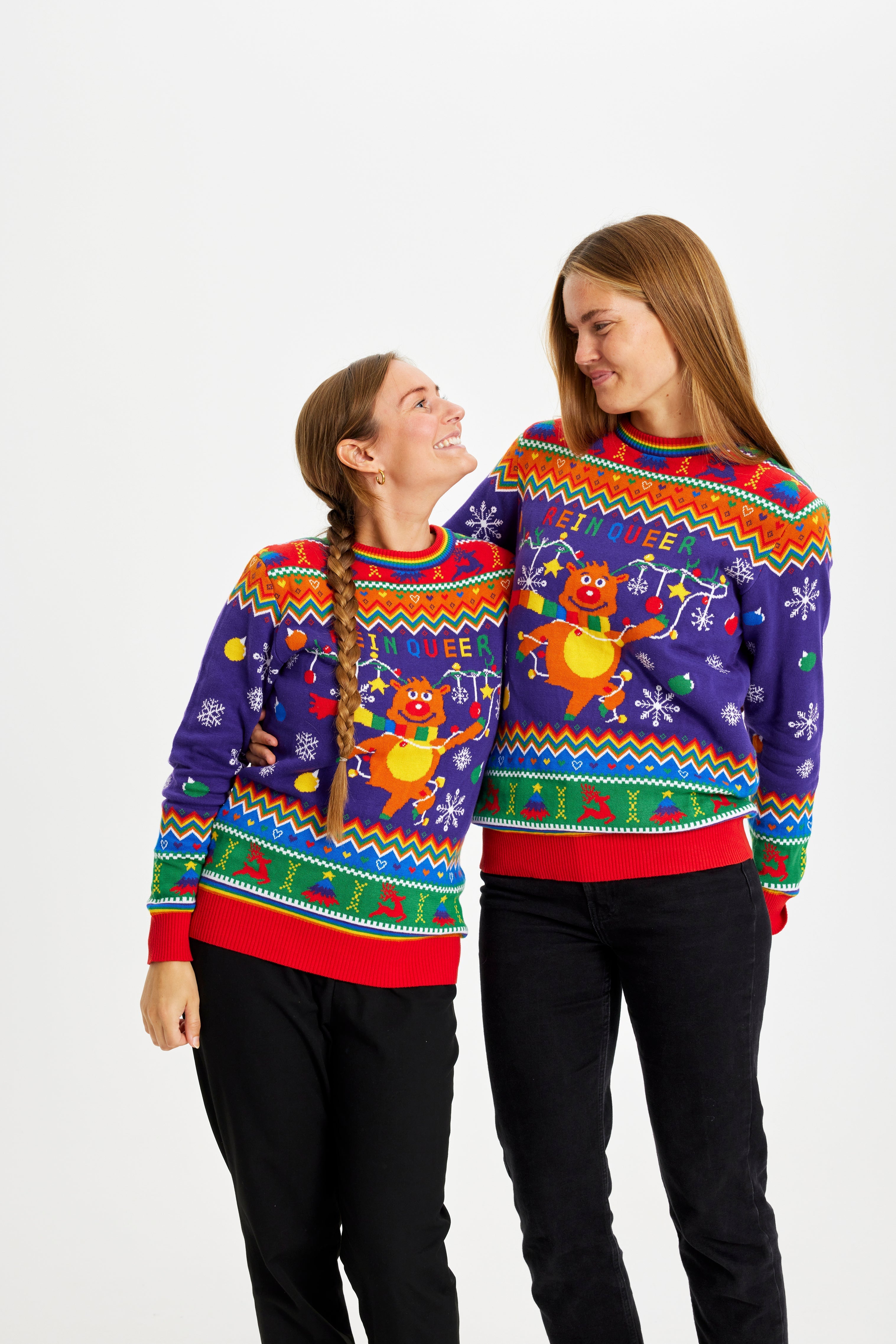 Zwei Frauen sehen sich an, die einen regenbogenfarbenen Weihnachtspulli mit dem Spruch